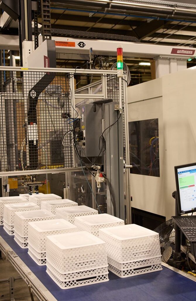 Stacks of white molded plastic baskets on a conveyor at a robotic molding cell
